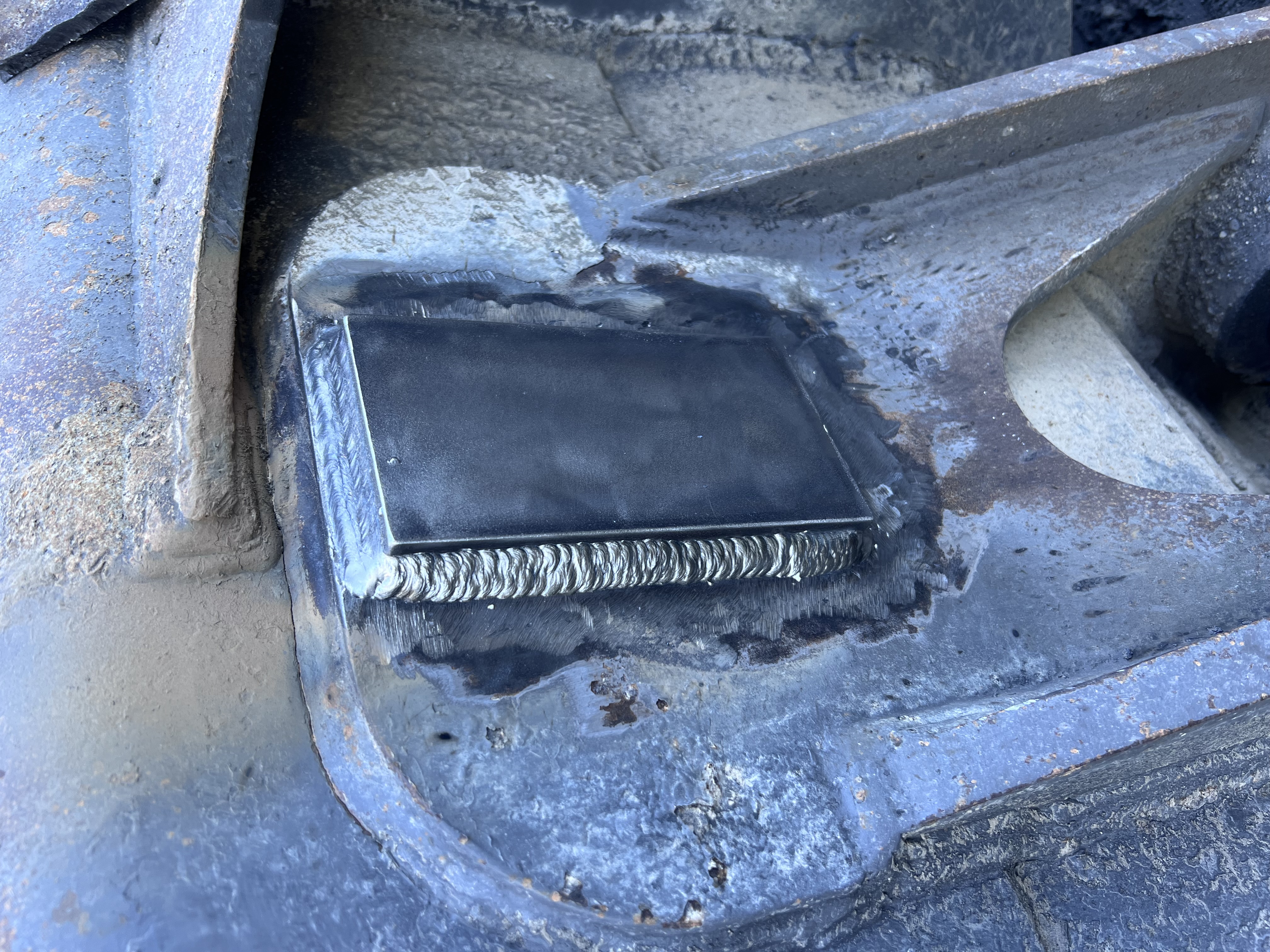 Close-up showing a significant weld repair on a thick, dark cast metal part (likely heavy equipment). Example of cast iron repair.